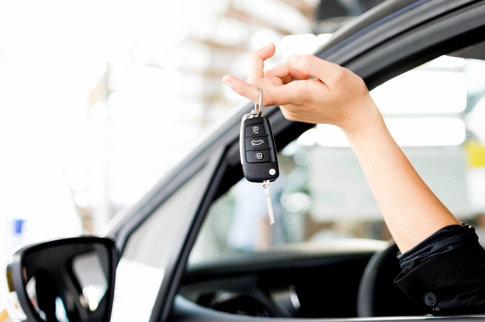 A person holding keys to their car in the drivers seat.