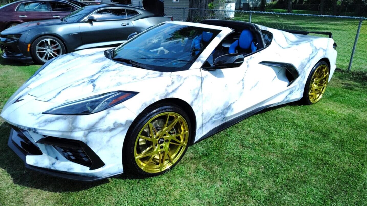 A white sports car with gold rims parked in the grass.