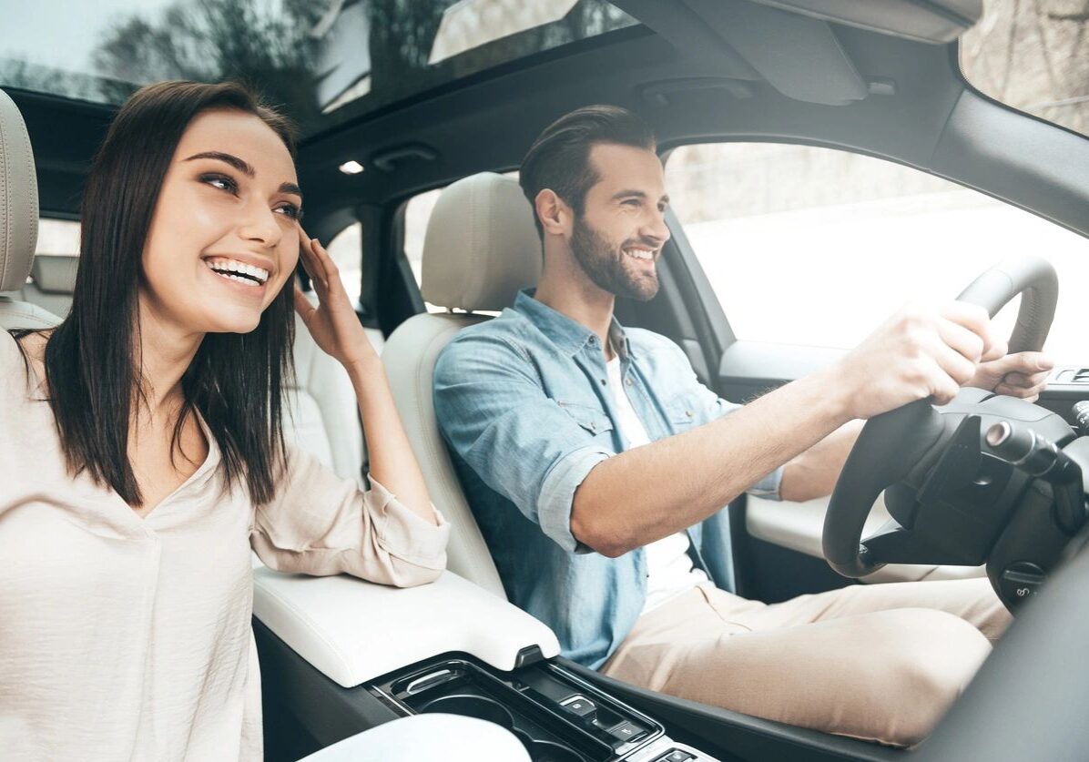 A man and woman sitting in the driver 's seat of a car.